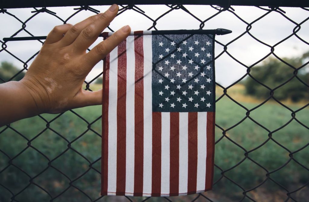 Mano sosteniendo la bandera de Estados Unidos, aumentan las deportaciones en 6 meses.